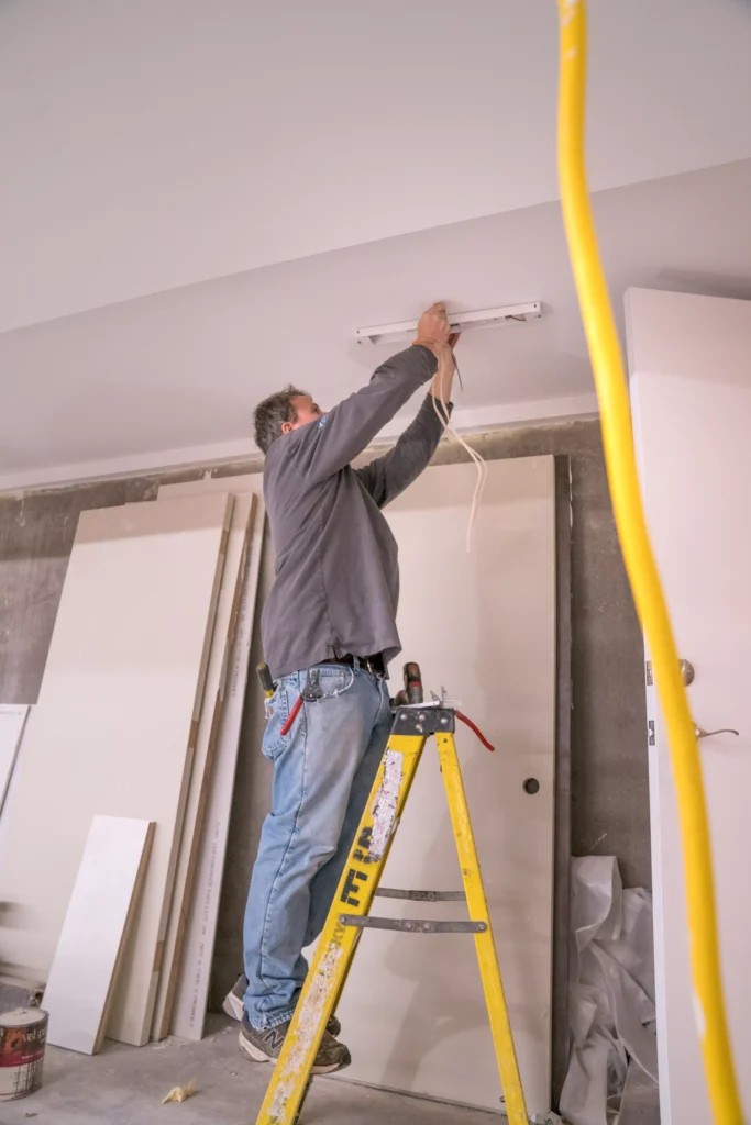 a person stands on a yellow ladder, installing or fixing a light fixture on the ceiling in minneapolis, mn.